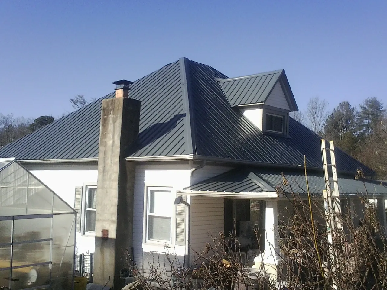 Dark blue standing seam metal roof on a white farmhouse with dormer — Slate & Tile Roof Repair by Roofing Brothers in Nixa