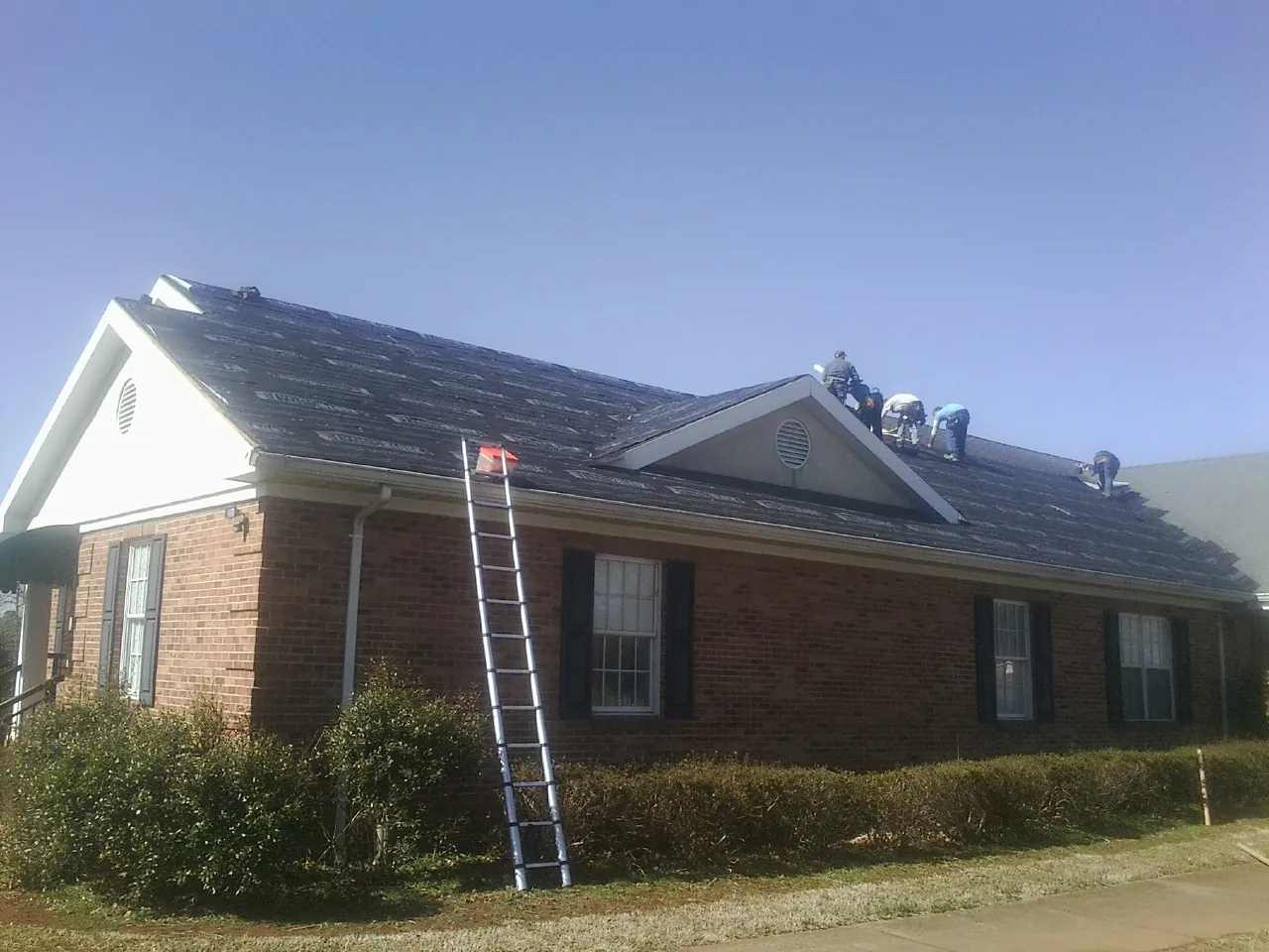 Crew tearing shingles off a brick ranch roof with a ladder set — Emergency Roof Repair work by our crew in Nixa