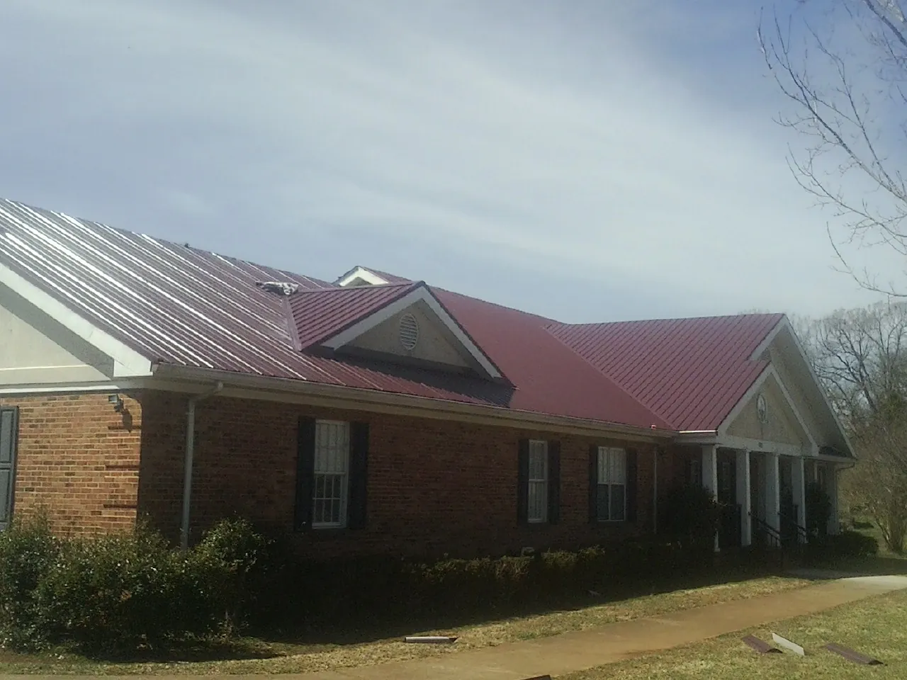 Red metal roof with gabled entries on a long brick building, from a Hail Damage Roof Repair job in Nixa
