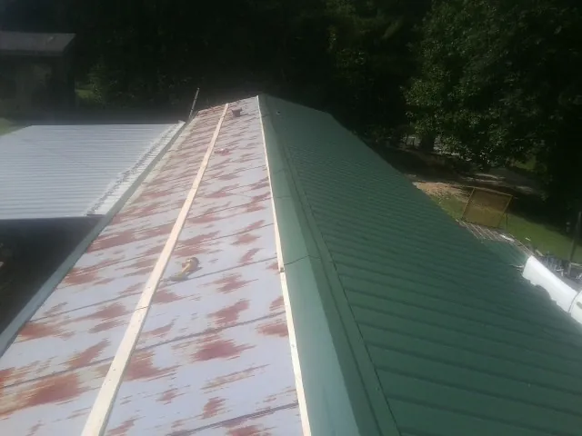 Old rusted panels beside newly installed green metal roofing — Wind Damage Roof Repair by Roofing Brothers in Nixa