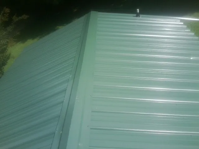 New green metal panels meeting at the ridge of a roof — Flat Roof Repair work by our crew in Nixa