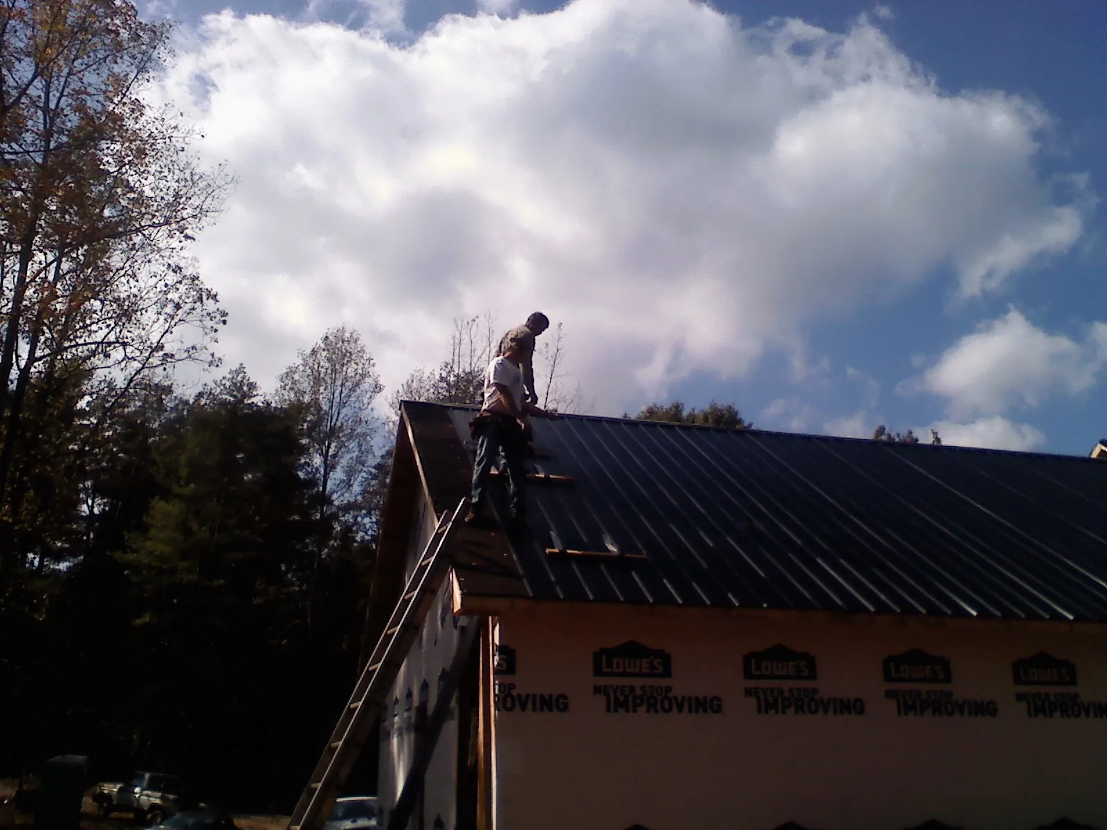 Roofer fastening dark metal panels high against a cloudy sky, from a Roof Inspection job in Nixa