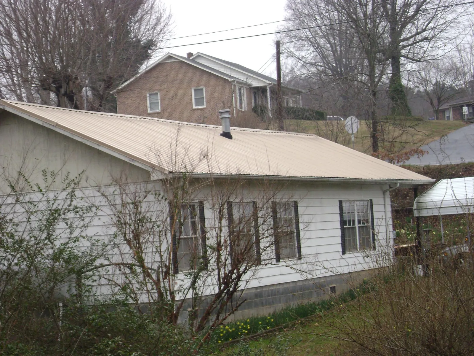 Tan metal roof on a white sided house set into a hillside — Commercial Roofing by Roofing Brothers in Nixa