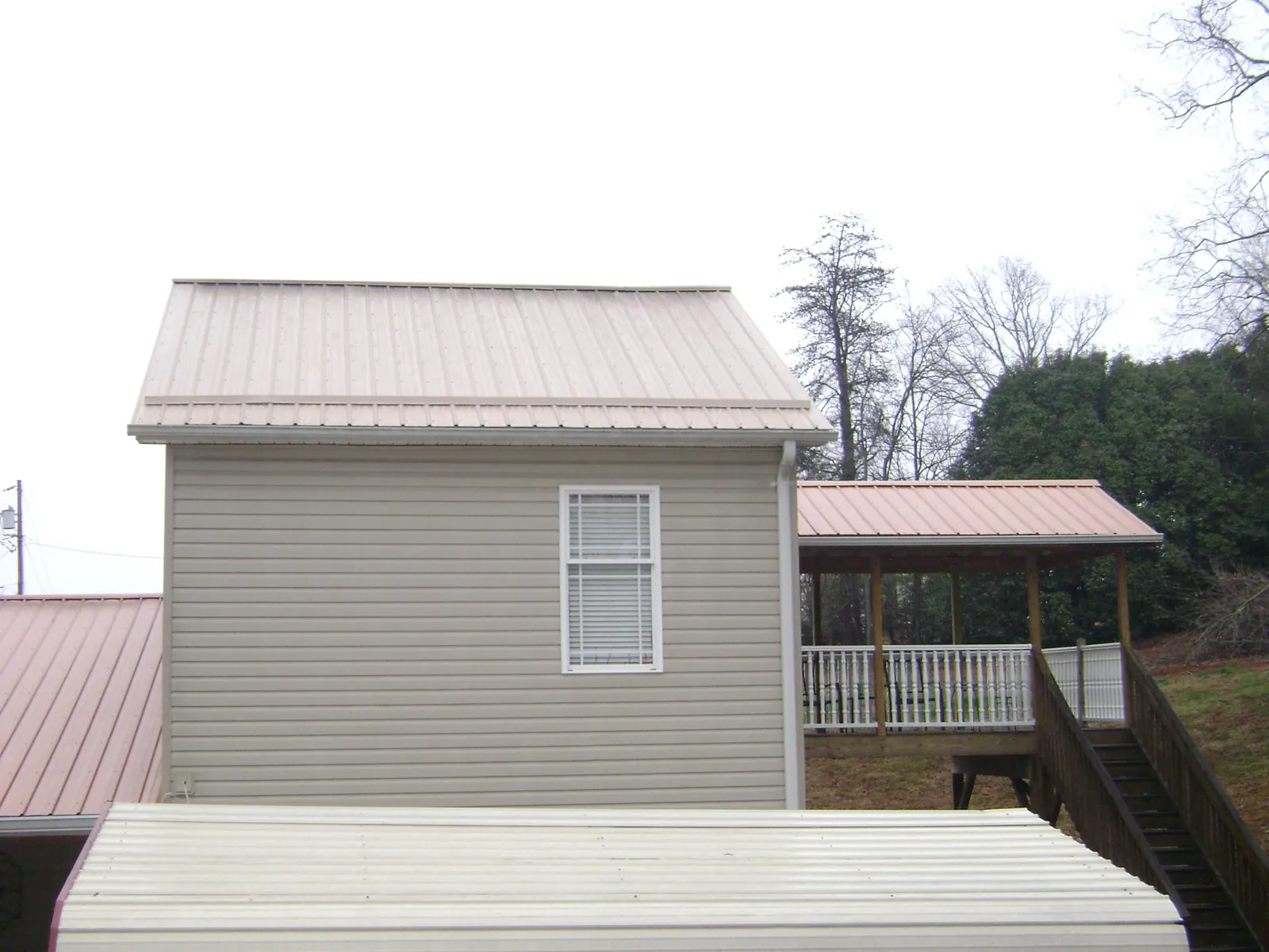 Tan metal roofs on a two story addition and attached porch, from a Roof Replacement job in Nixa